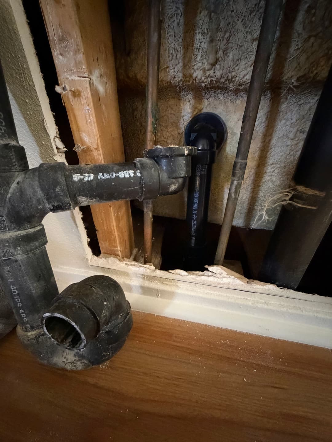 Visible plumbing pipes and fittings behind a wall with wood framing and insulation.