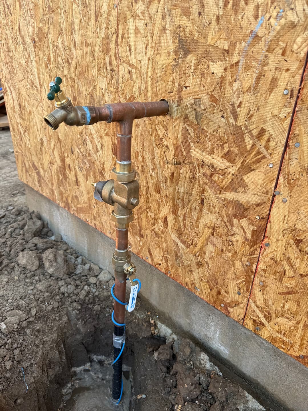 Water supply plumbing installation with copper pipes and valves next to an unfinished wall.