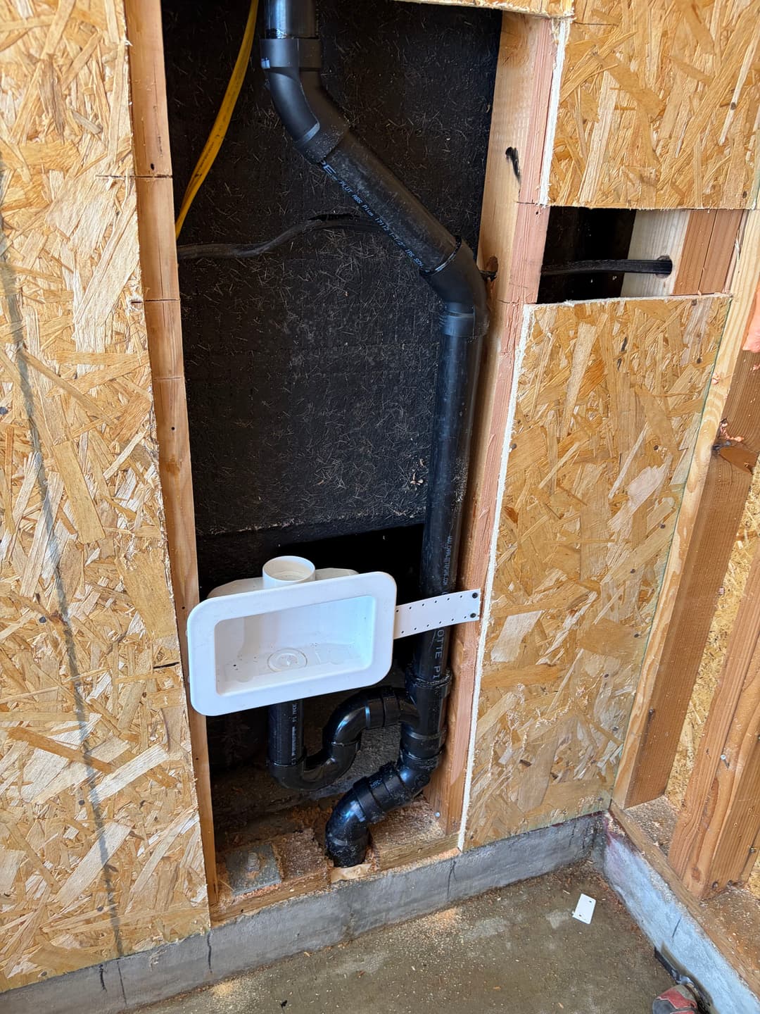 Inside view of a plumbing installation showing PVC pipes and a sink drain in a wall.