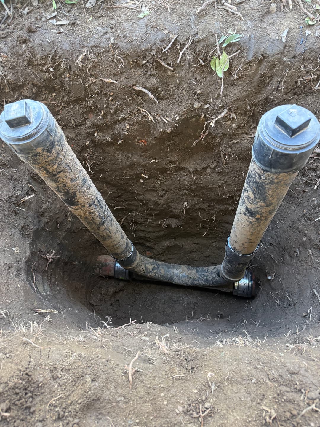Exposed underground water pipes in a dirt trench highlighting plumbing installation.