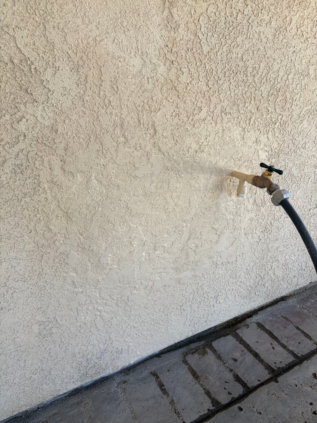 Exterior wall featuring a water faucet and hose connection for irrigation purposes.