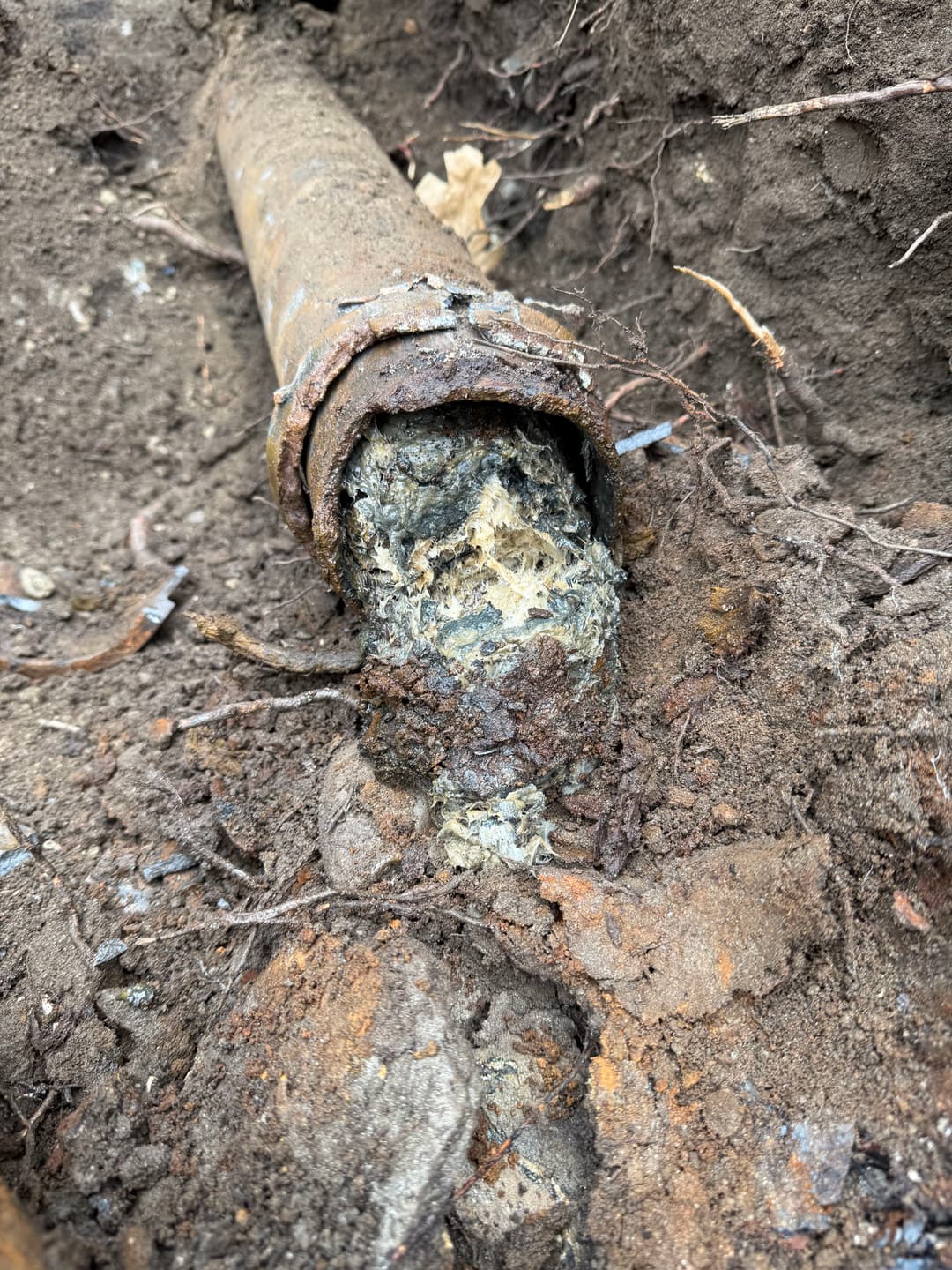 Corroded pipe with buildup and soil surrounding it, indicating potential plumbing issues.