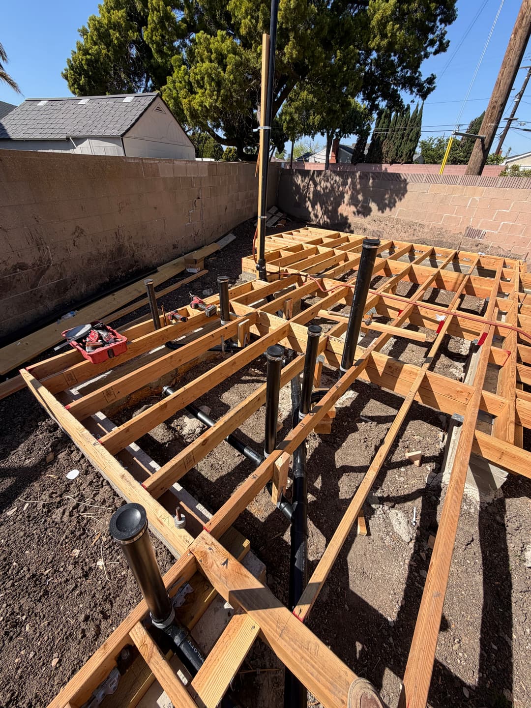Construction site with wooden framing and plumbing pipes laid out on the ground.
