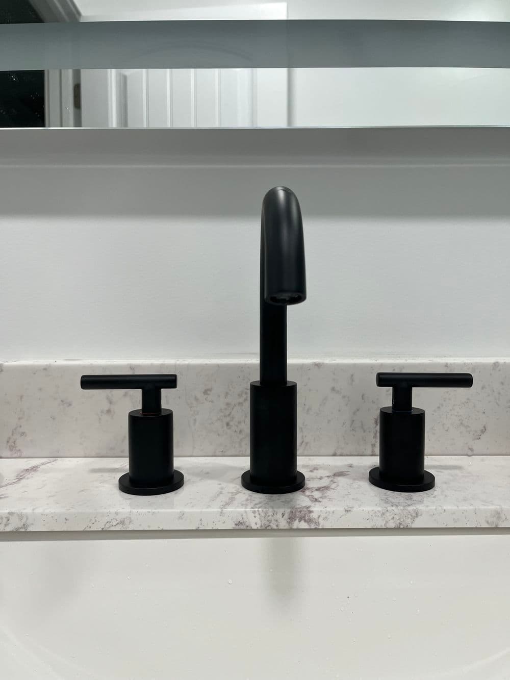 Black modern bathroom faucet set with two knobs on a marble countertop.