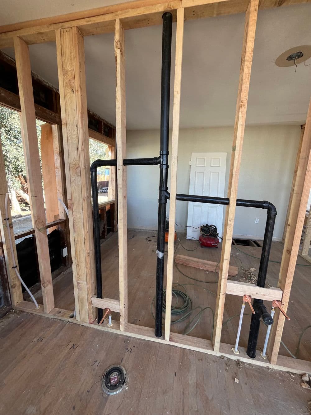 Interior home renovation showing exposed plumbing pipes and framing details.